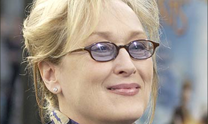 Person wearing black rectangular eyeglasses with a silver nose bridge and a smile, with blonde hair pulled back.
