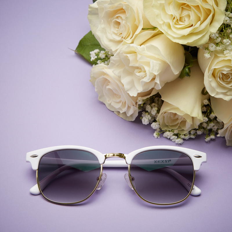 White-framed sunglasses with dark lenses by Zenni, placed next to a bouquet of white roses.