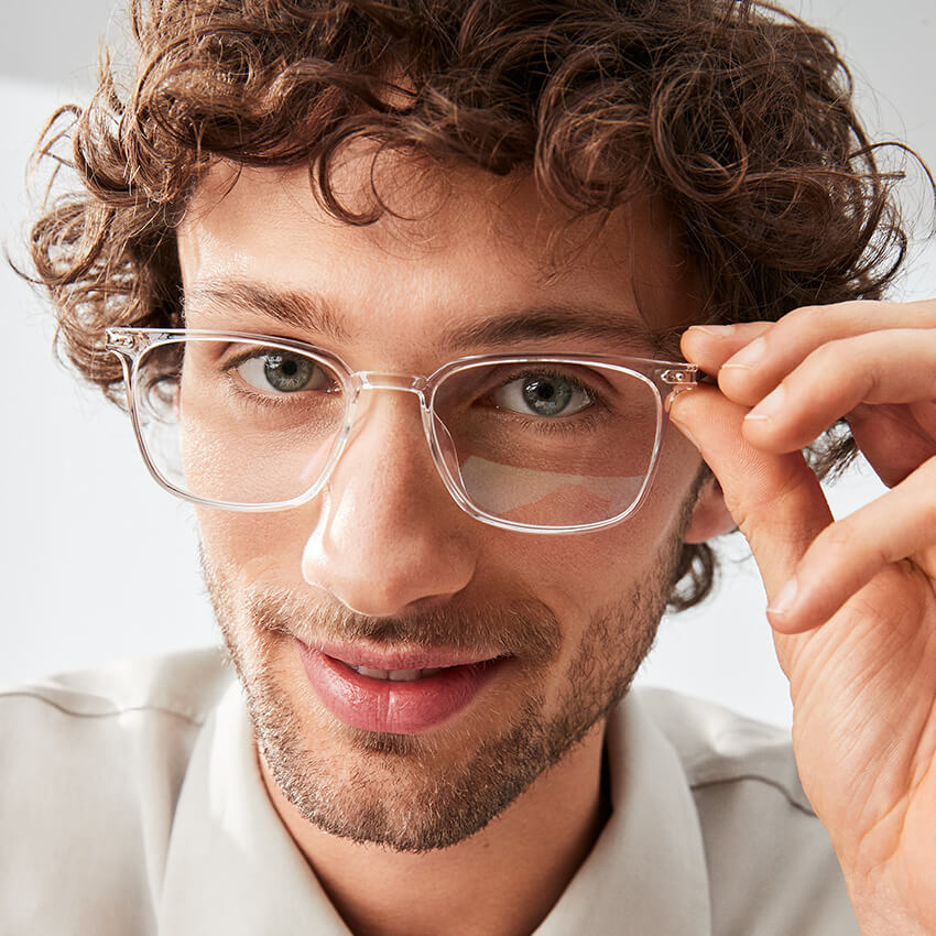 Man wearing clear prescription eyeglasses, gently adjusting the frame with his right hand.