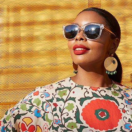Woman wearing sunglasses with clear frames, large round earrings, and a floral patterned shirt.