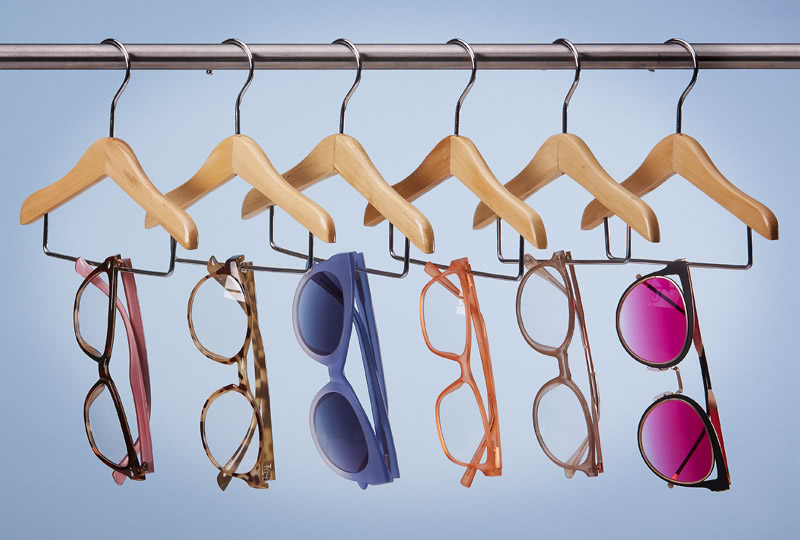 Eyeglasses and sunglasses hanging from wooden hangers on a clothes rack.