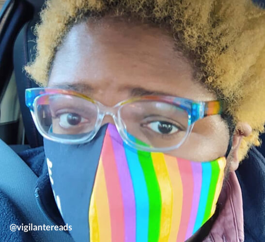 Person wearing a colorful rainbow-striped face mask and transparent rainbow glasses. Text: @vigilantereads