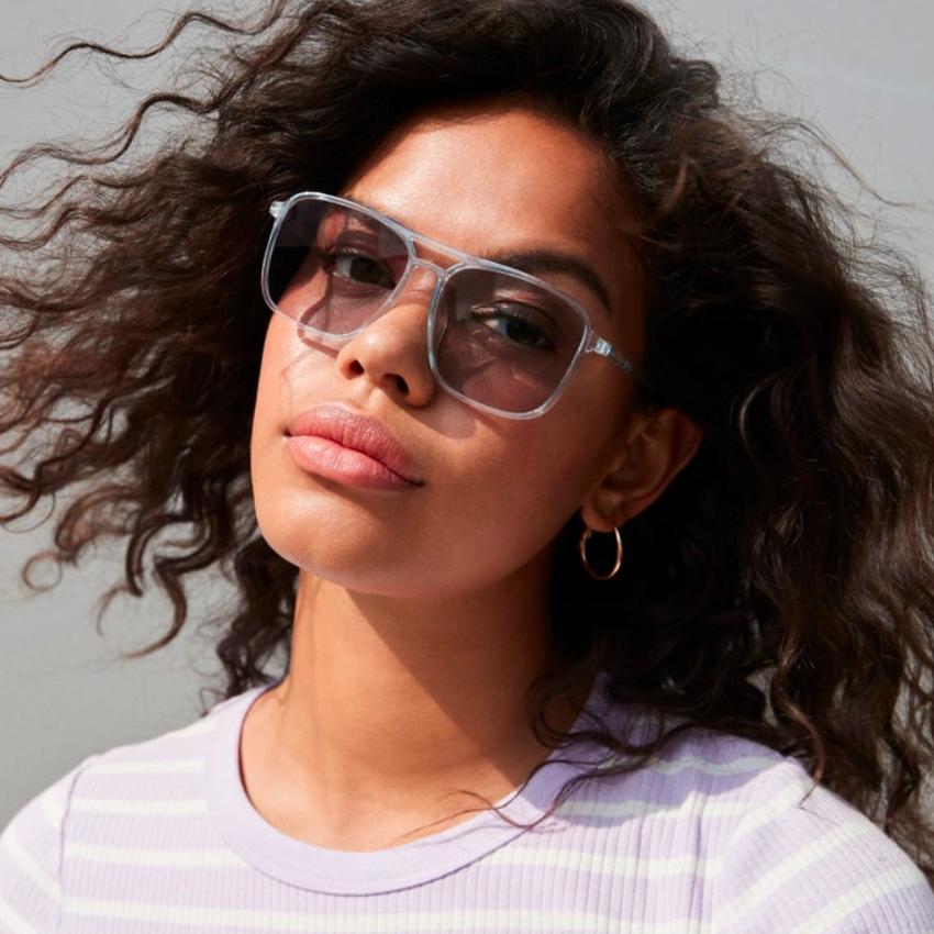 Woman wearing light blue translucent sunglasses and a light purple striped shirt.