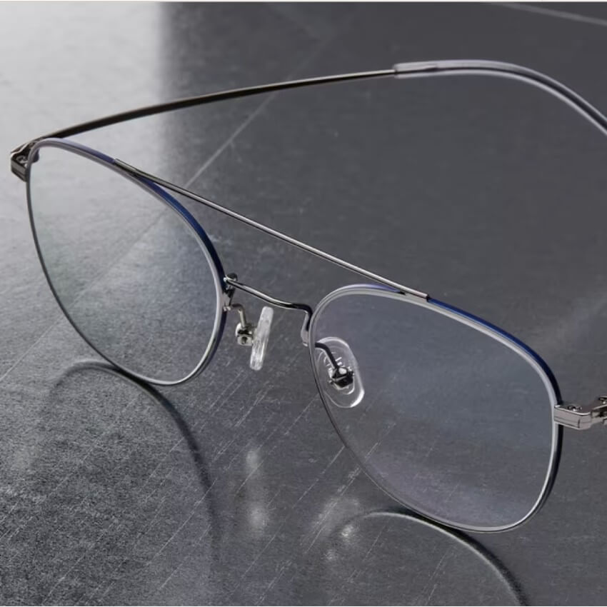 Thin, metal-frame eyeglasses with oval lenses on a reflective surface.