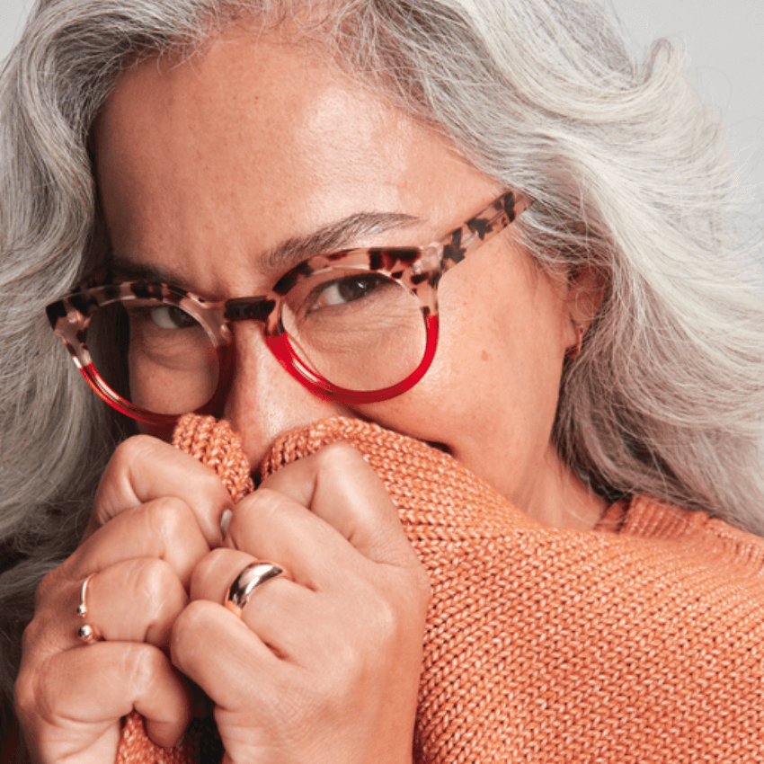 Woman wearing red and tortoiseshell eyeglasses, holding an orange knit sweater close to her face.