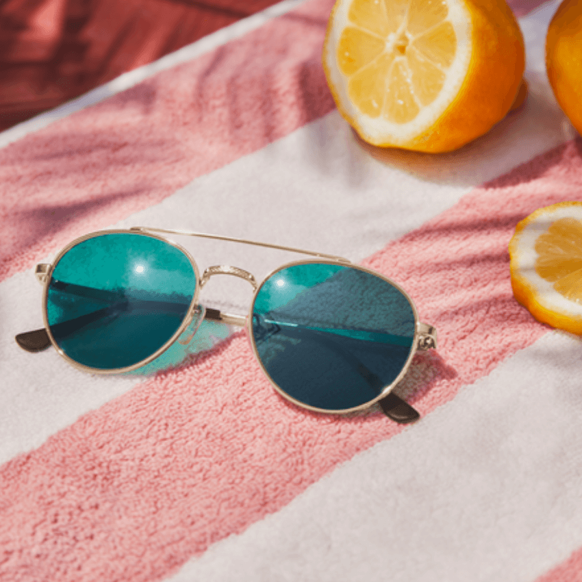 Round sunglasses with reflective blue lenses on a pink and white striped towel, next to lemon slices.