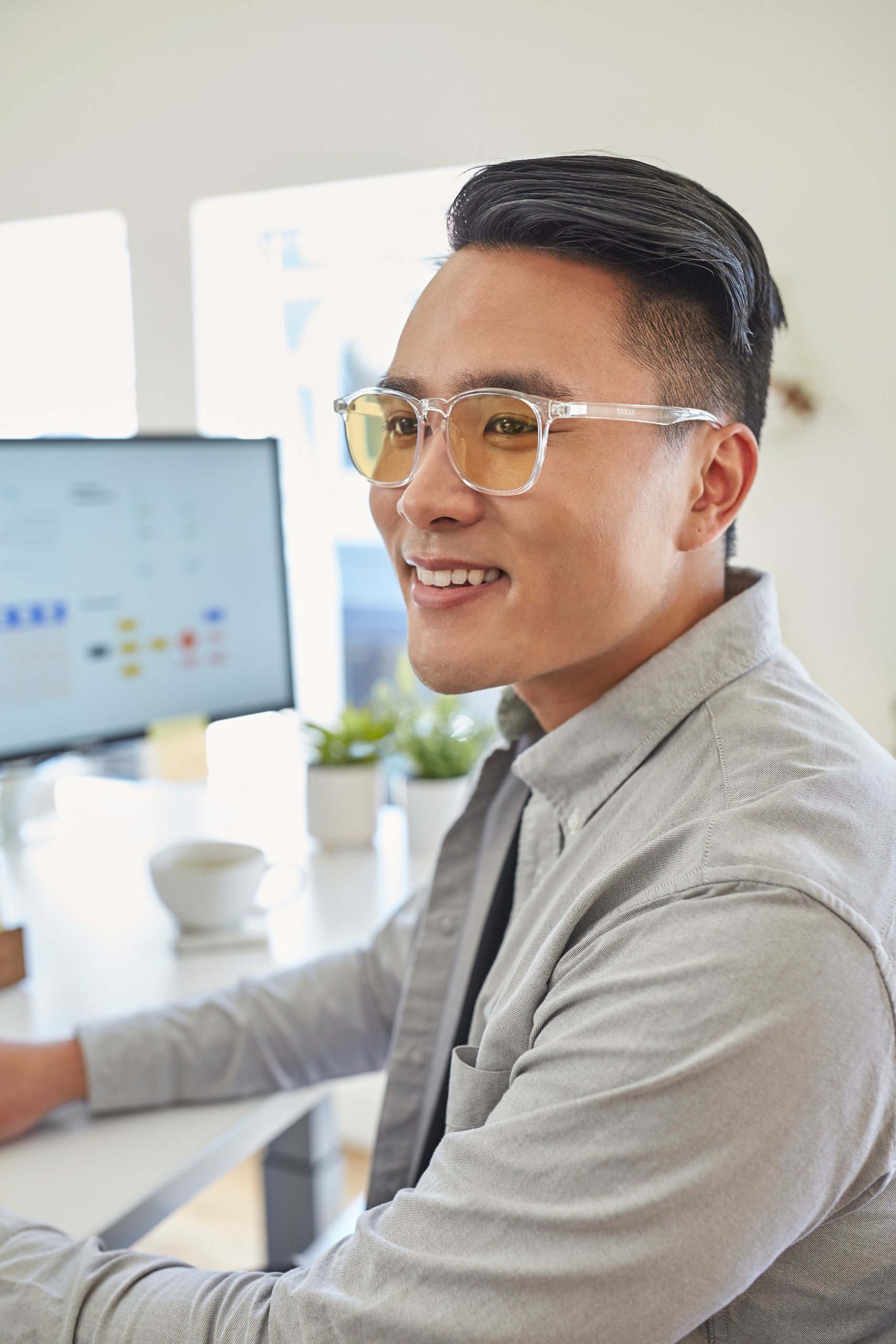 Man wearing clear-framed glasses with yellow-tinted lenses, smiling while working at a computer desk.