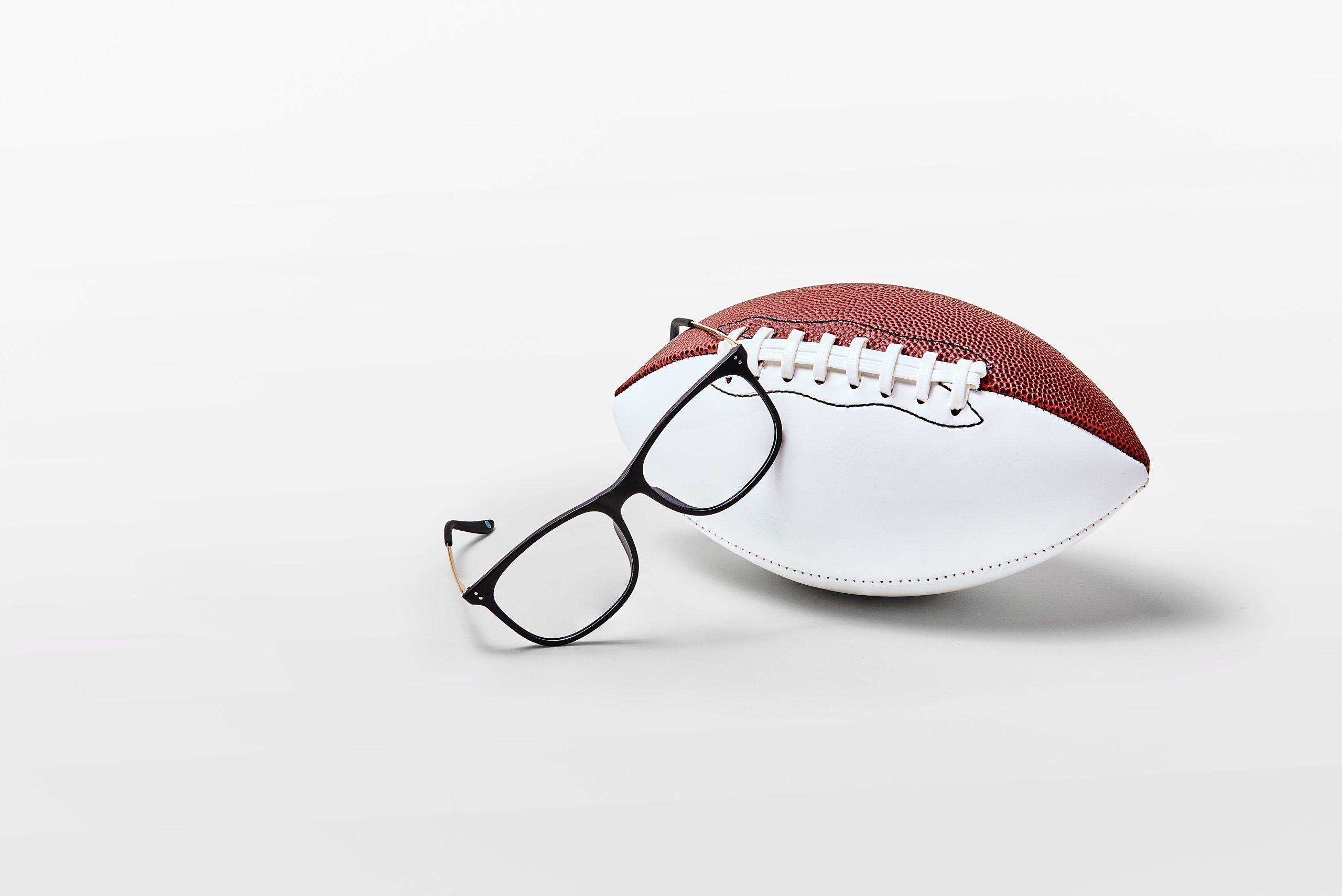 Football placed beside black rectangular eyeglasses on a white background.