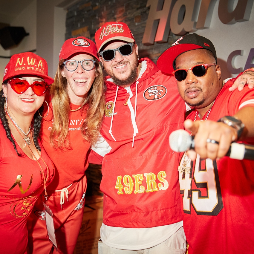 Four people wearing San Francisco 49ers gear, including hats, shirts, and jackets.