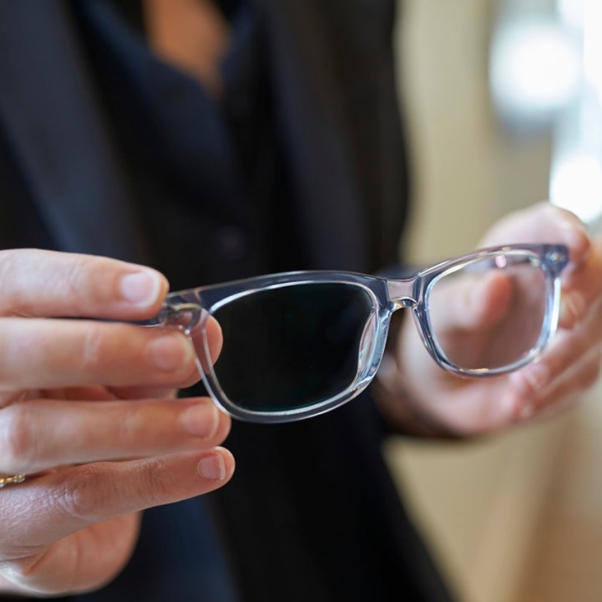 A person holding clear, rectangular eyeglasses with a blue tint.