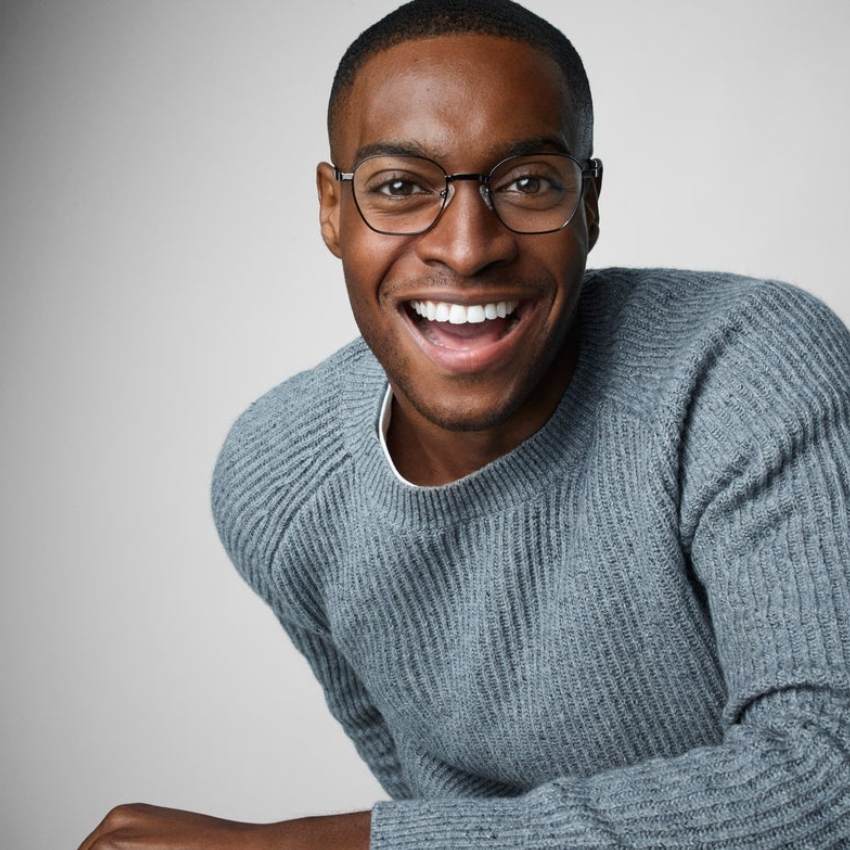 Man wearing a gray sweater and stylish glasses, smiling broadly.