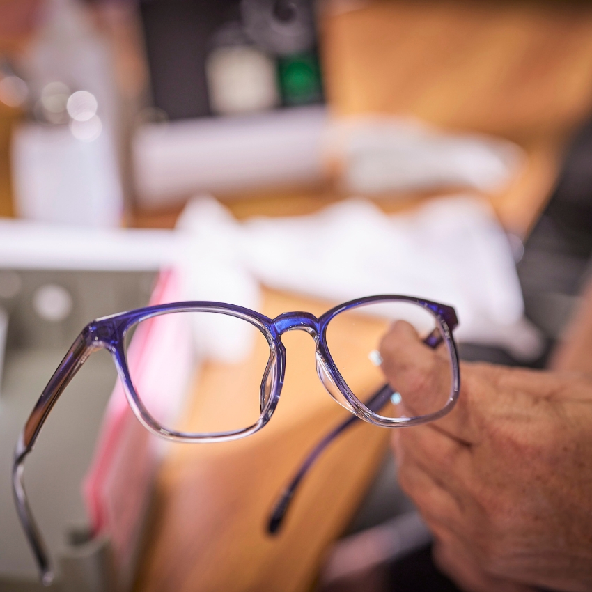 Blue eyeglasses held by a hand.