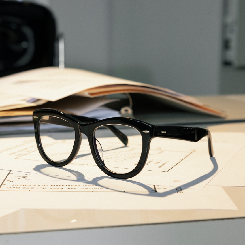 Black rectangular eyeglasses with thick frames resting on a stack of papers.