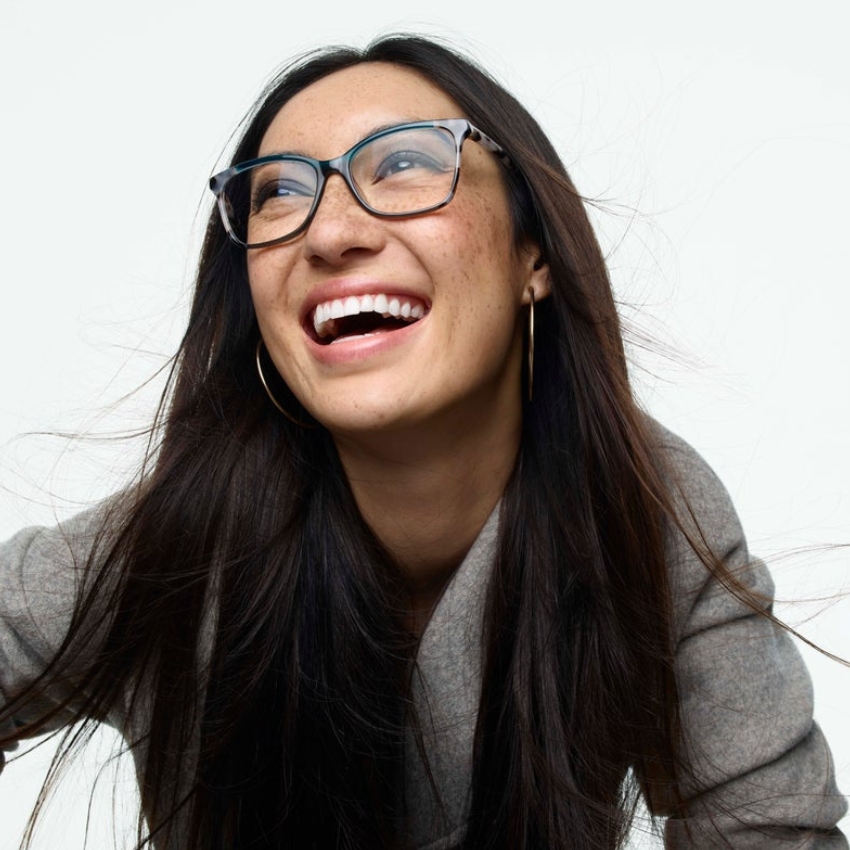 Glasses with clear blue frames and grey temples worn by a person smiling and looking upwards.