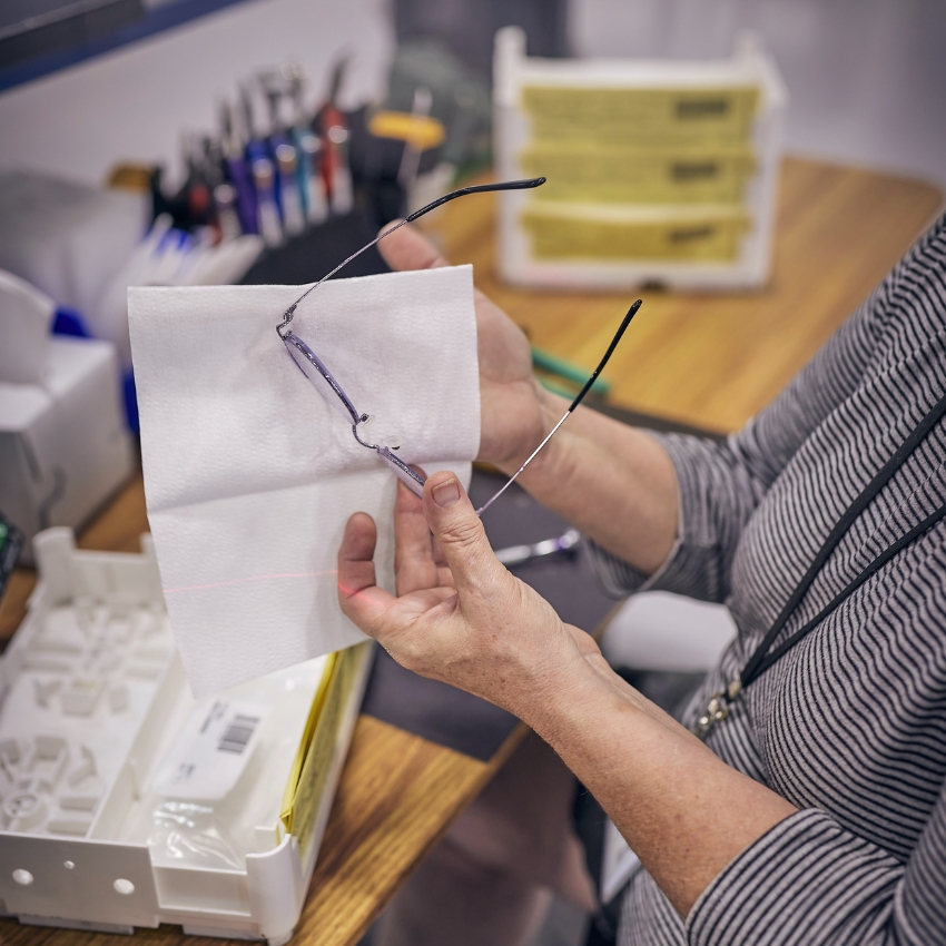 Hands holding and cleaning eyeglasses with a white cloth.