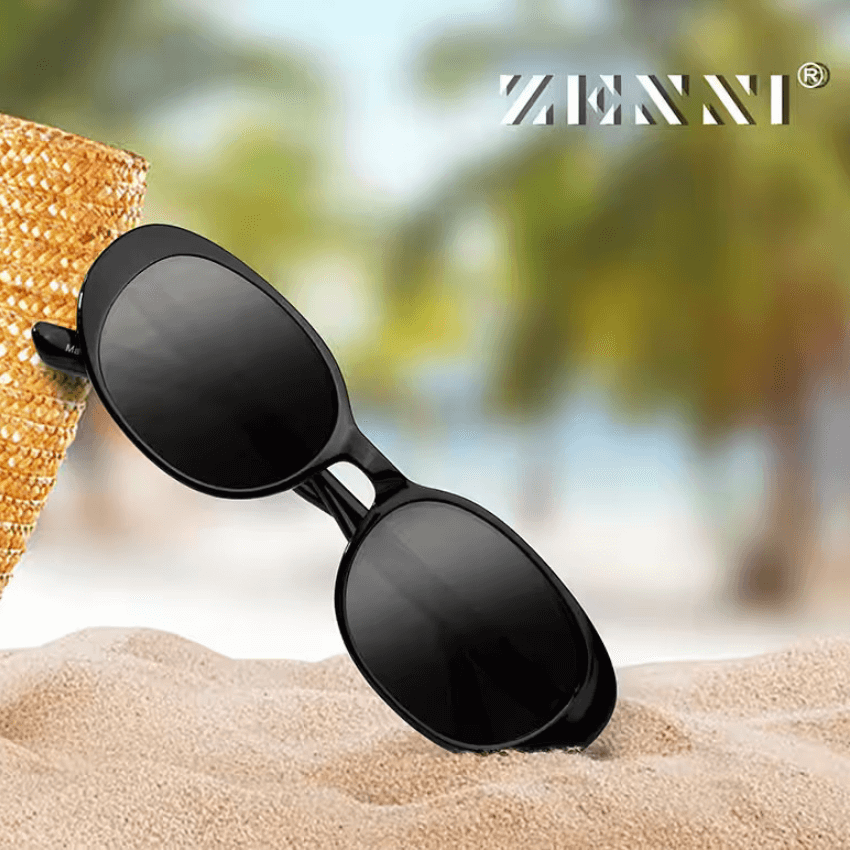 Black Zenni sunglasses resting on sand, branded with "ZENNI" in the top right corner.