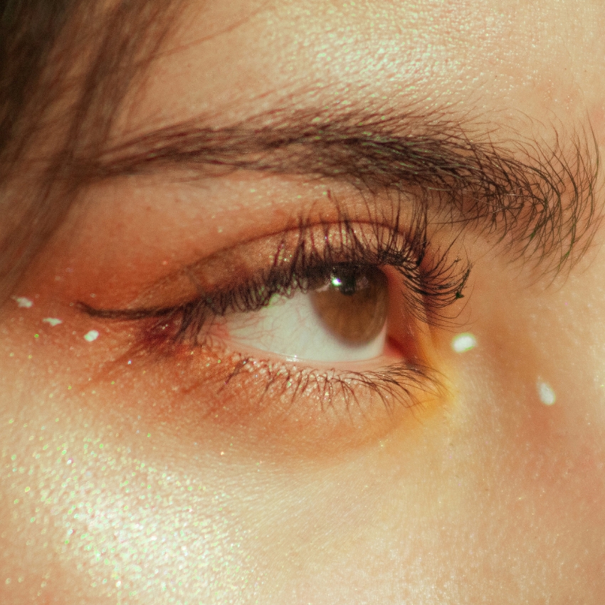 Close-up of a brown eye with light peach and gold eyeshadow and a few white makeup dots around it.