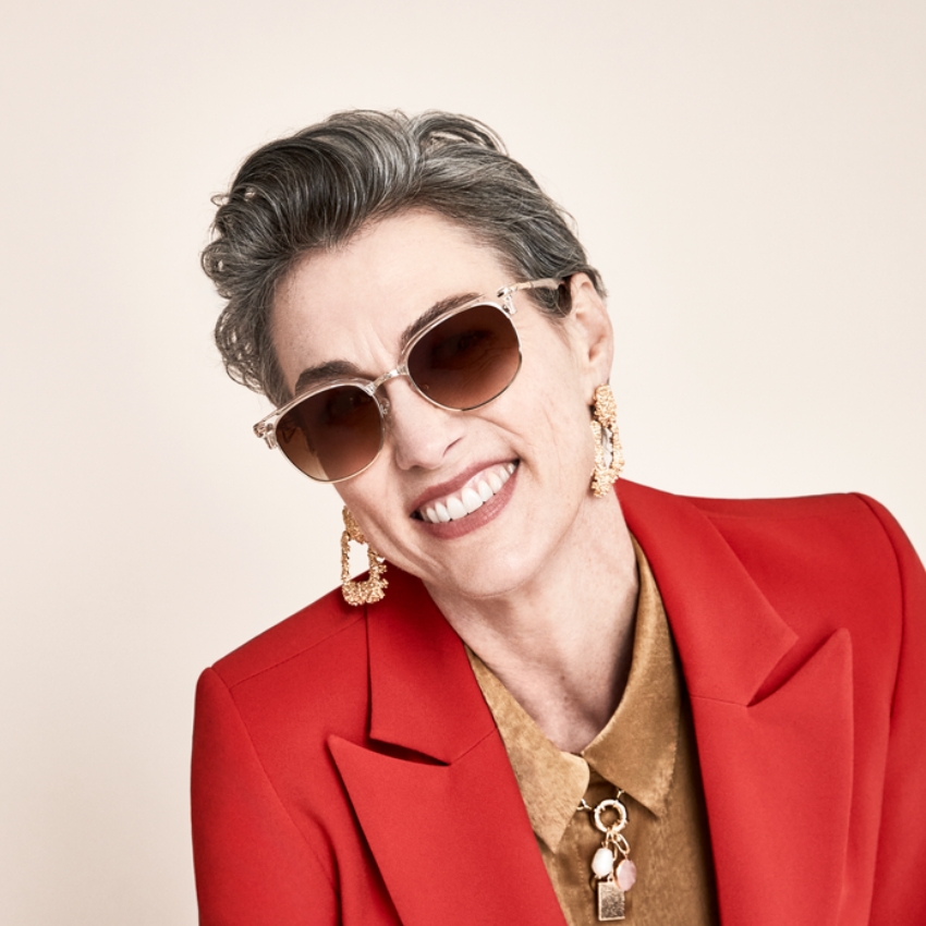 Sunglasses with light brown lenses and a clear frame, worn with gold earrings and a red blazer.