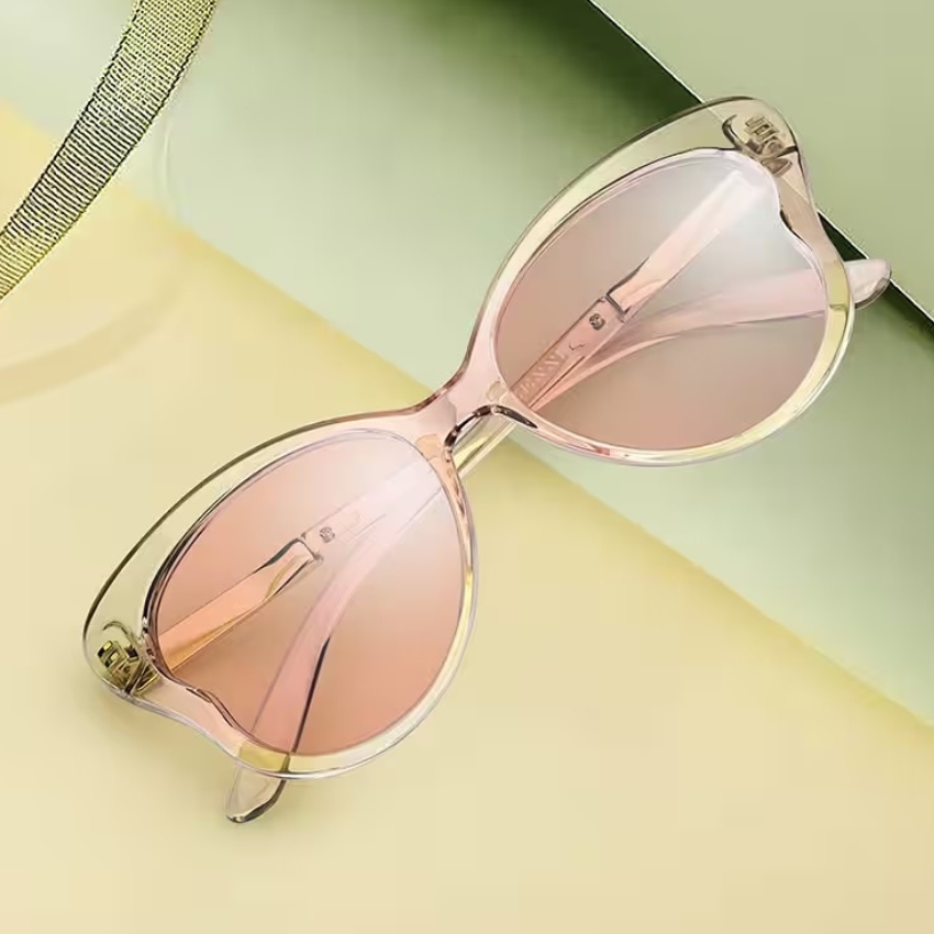 Translucent pink cat-eye sunglasses with mirrored lenses and yellow accents on a pastel green and yellow background.