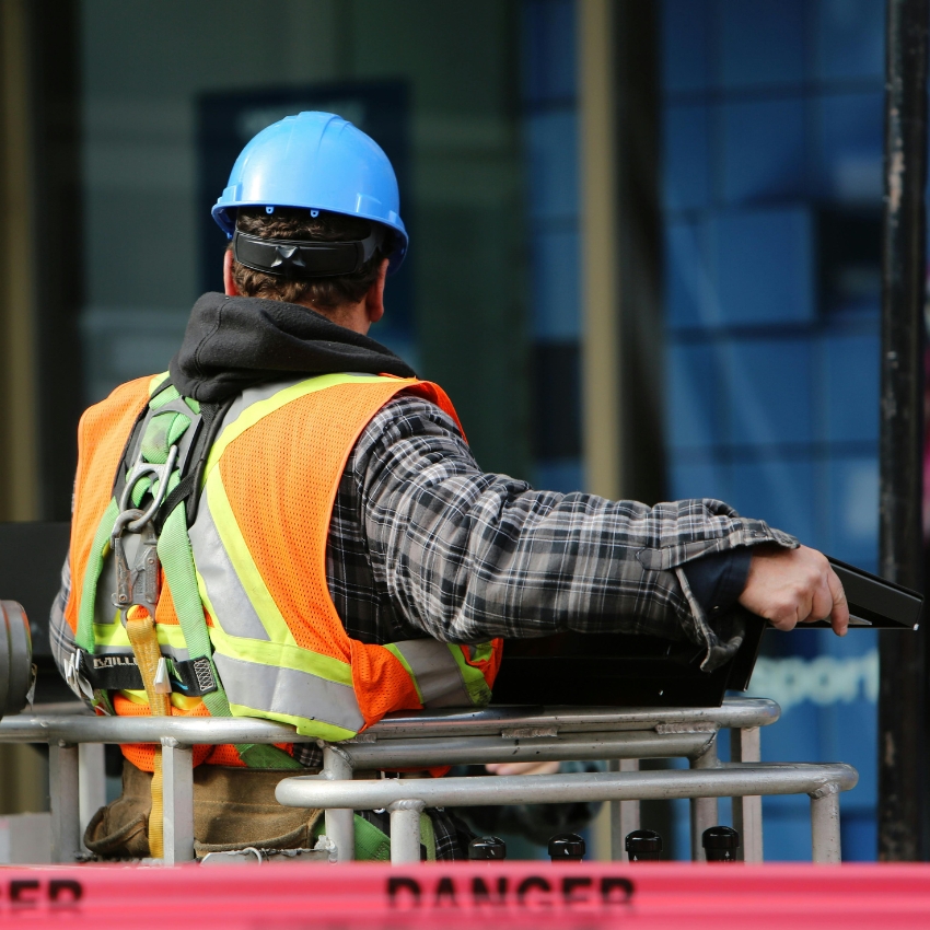 Construction worker in an orange safety vest and blue hard hat operating machinery.