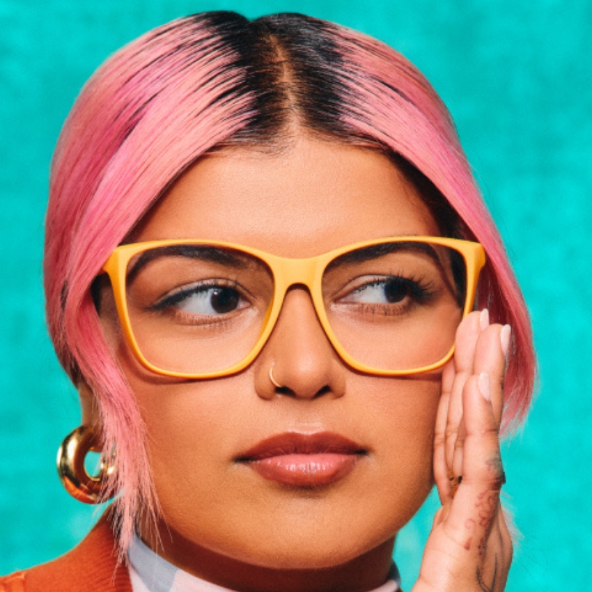 Bright yellow eyeglasses worn by a person with pink hair and gold hoop earrings.