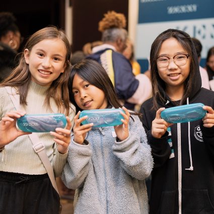 Three kids holding turquoise ZENNI cases with glasses inside.