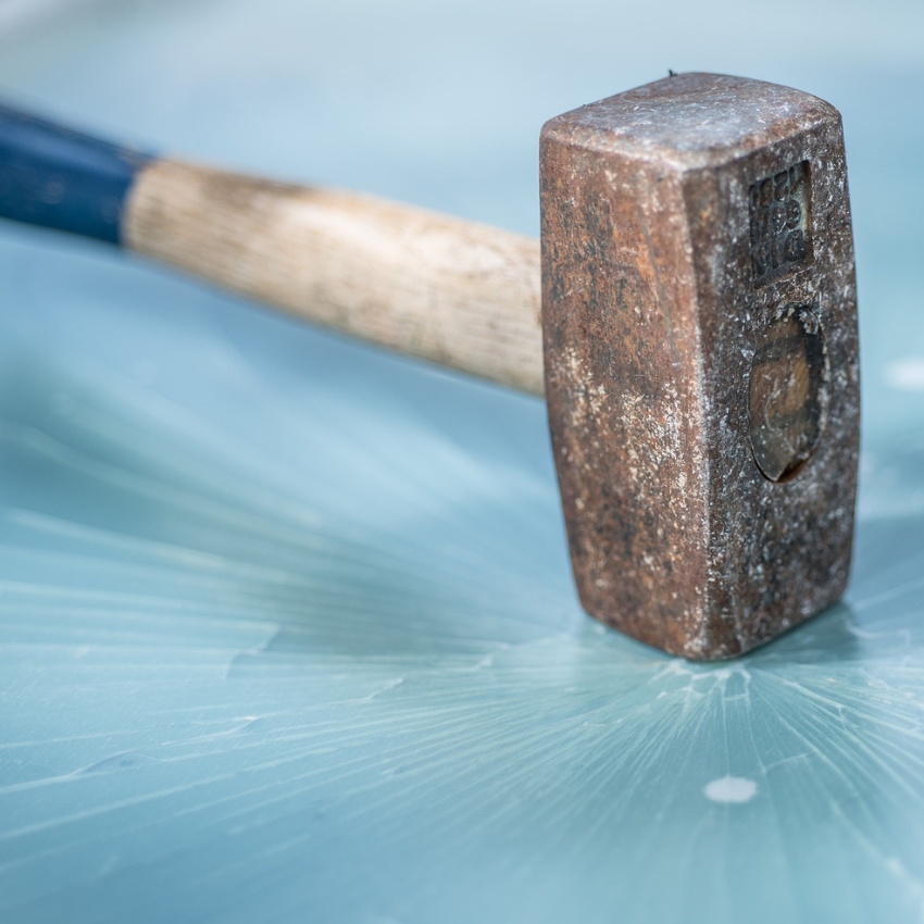 Rusty hammer with a wooden handle on a cracked glass surface.