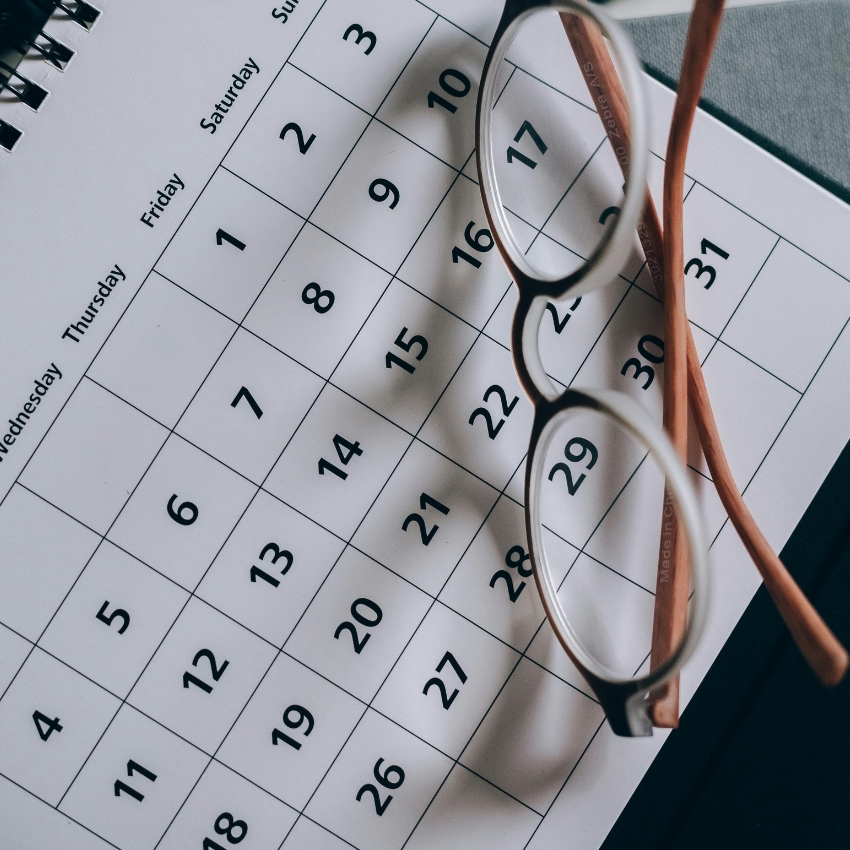 Spiral-bound calendar with dates and days of the week, eyeglasses placed on top.