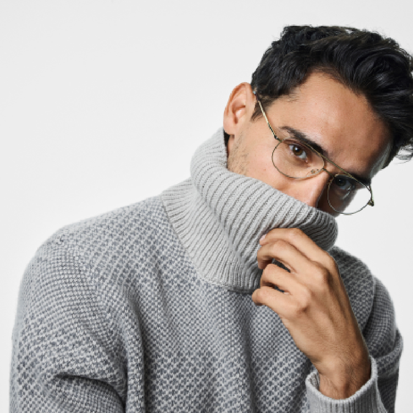 Man wearing a light gray turtleneck sweater and gold-rimmed glasses.