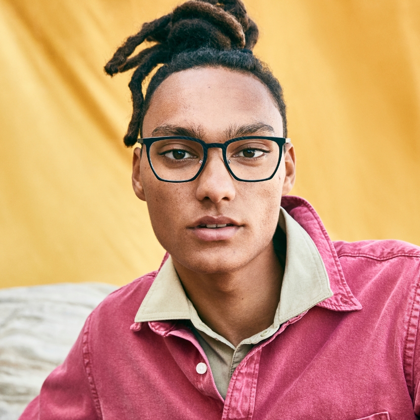 Person wearing black rectangular glasses with a pink shirt and beige inner collar.