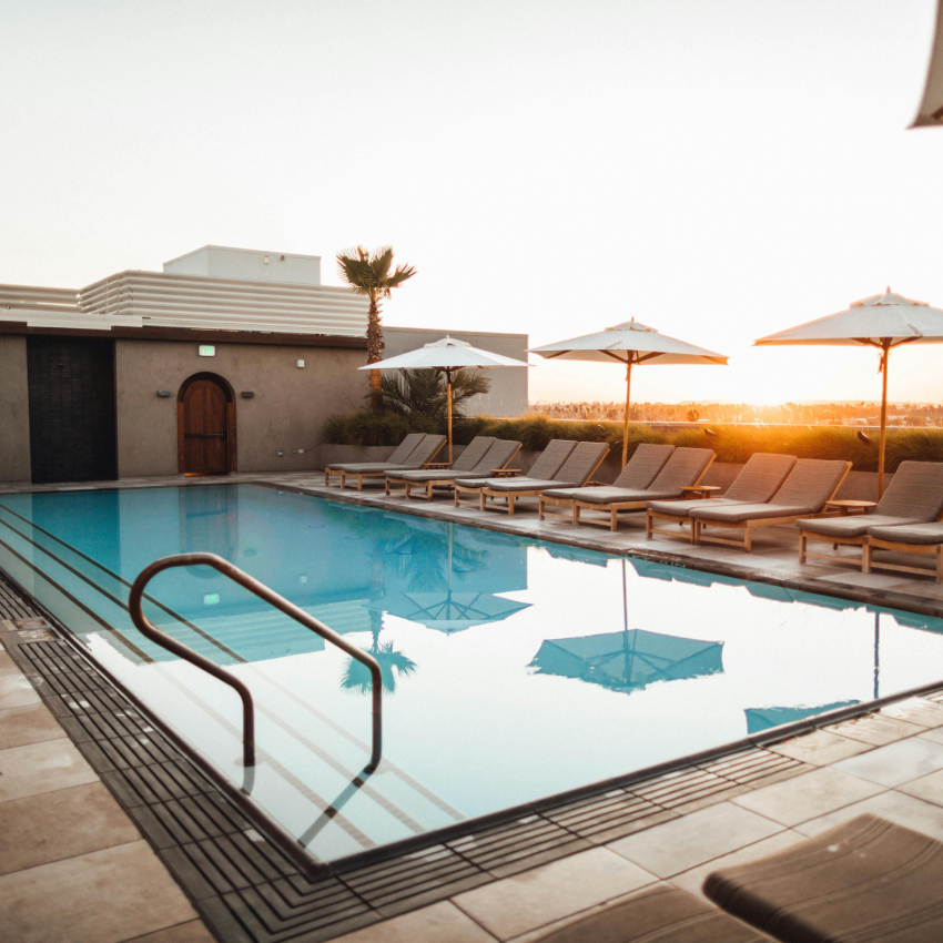 Poolside loungers under umbrellas beside a rectangular swimming pool with handrails.