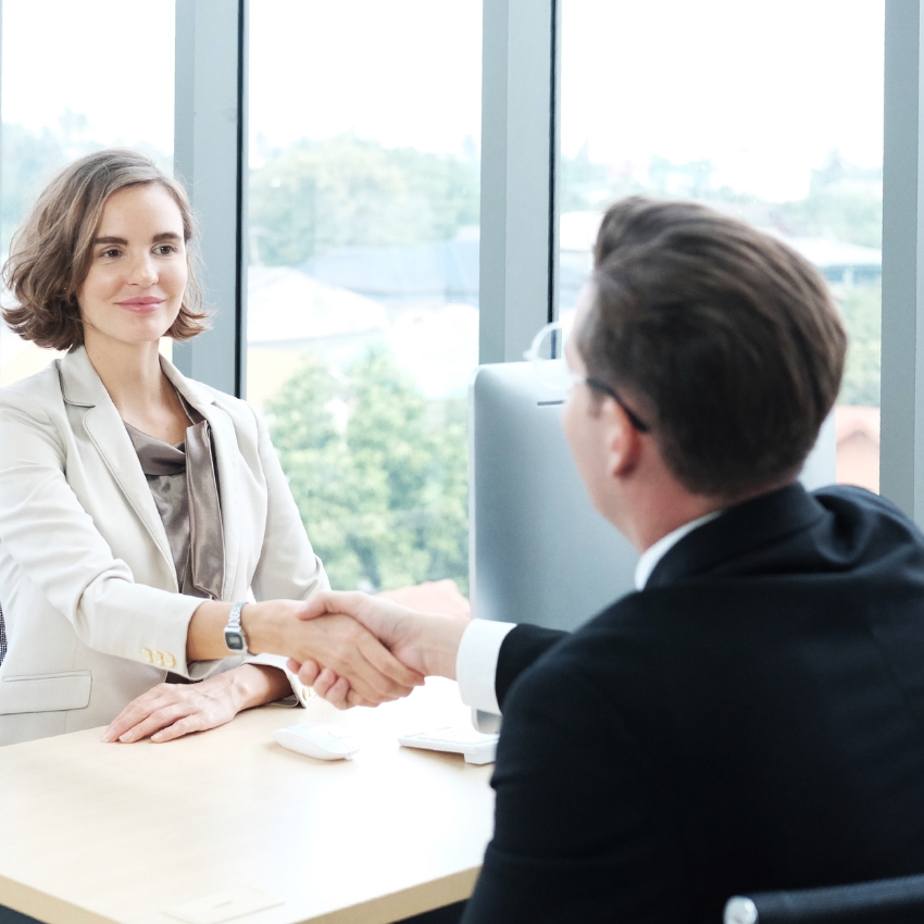 Business professionals shaking hands across a desk in a modern office.